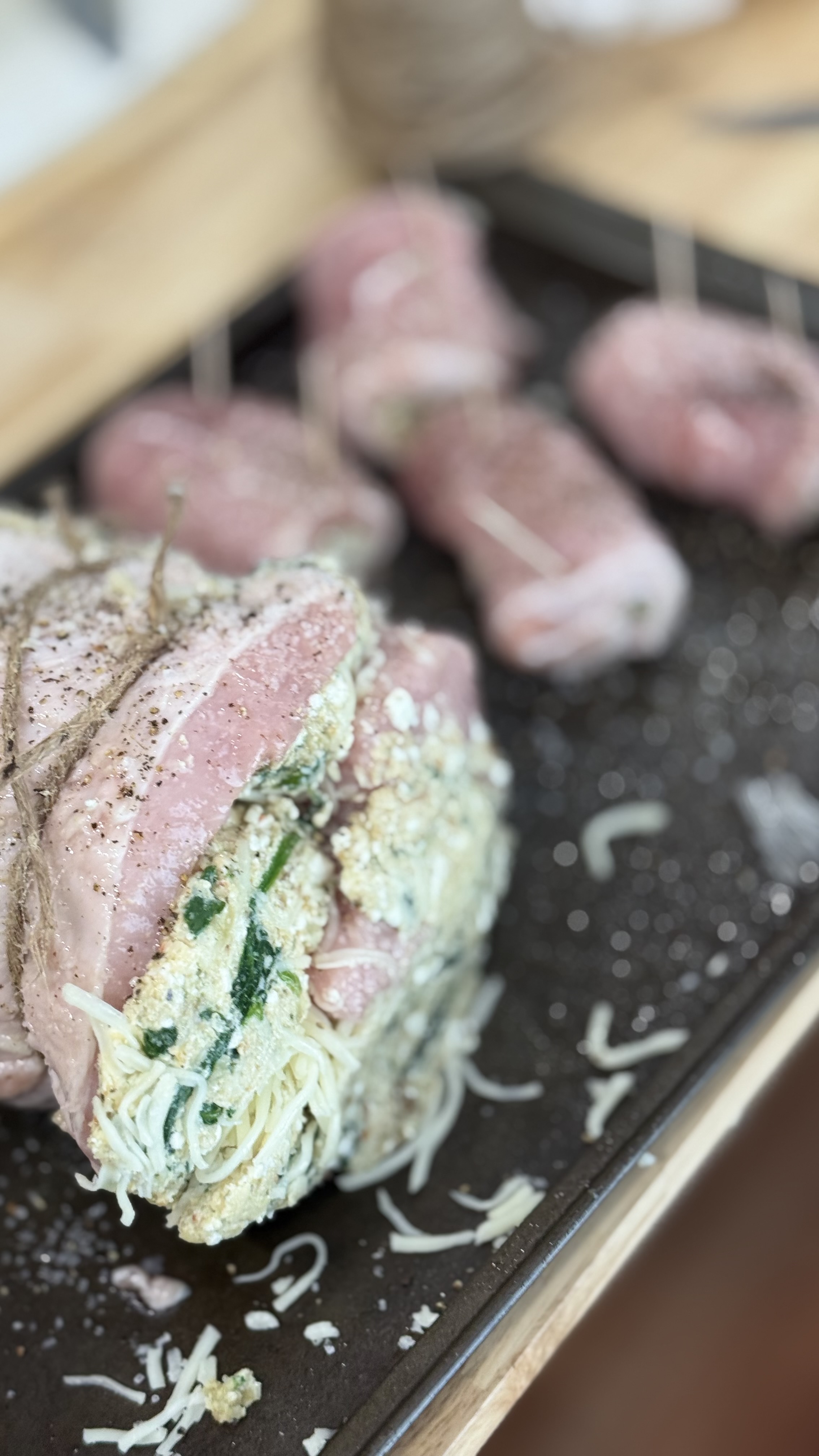 Raw pork loin rolled and tied with butcher's twine, the spinach, breadcrumb and mozzarella filling visible along the open seam