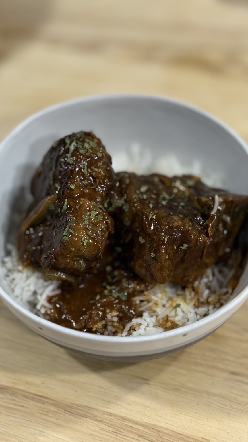 Finished braised lamb shoulder chops coated in glossy onion sauce and served over white basmati rice in a white bowl.