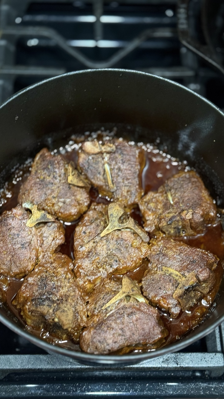Deeply browned lamb shoulder chops arranged in a Dutch oven with braising liquid before the covered oven braise.